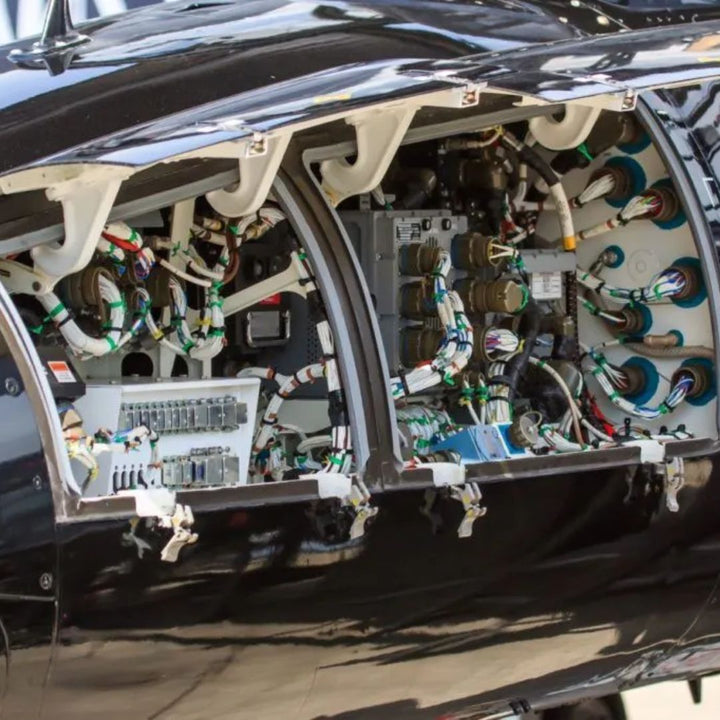 Interior view of a helicopter avionics bay with the panel open, showing densely routed wiring harnesses secured with cable ties, connectors, and bundled looms across the airframe structure.