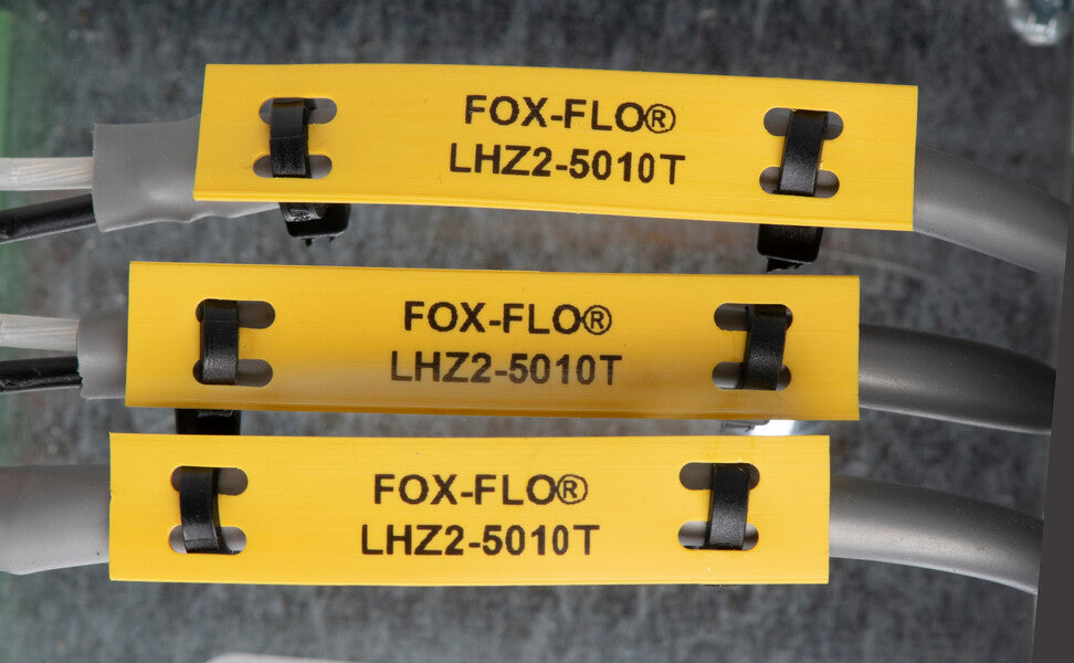 Three yellow cable identification labels reading “FOX-FLO® LHZ2-5010T” are attached to grey cables with black clips, stacked horizontally against a grey background.