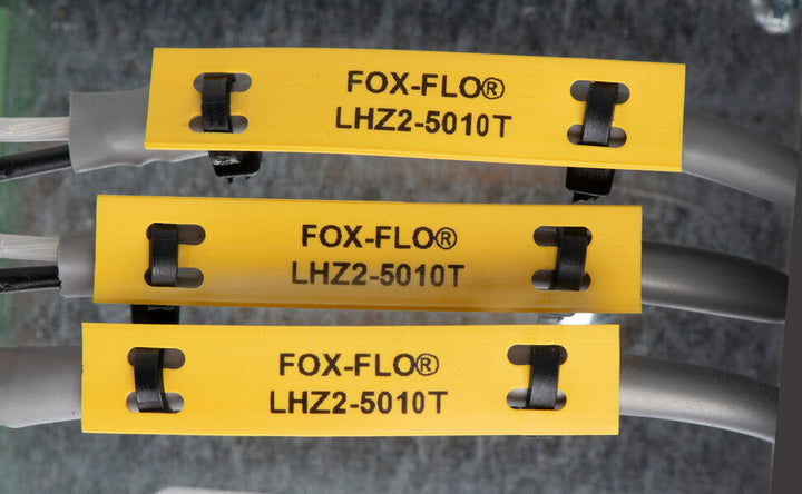 Three yellow cable identification labels reading “FOX-FLO® LHZ2-5010T” are attached to grey cables with black clips, stacked horizontally against a grey background.
