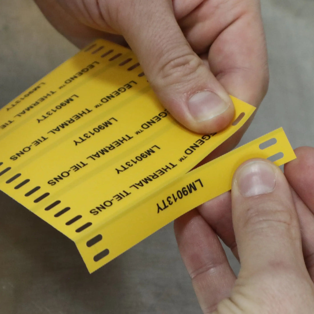 Hands peel a strip of yellow tie-on cable labels printed “LM9013TY”.