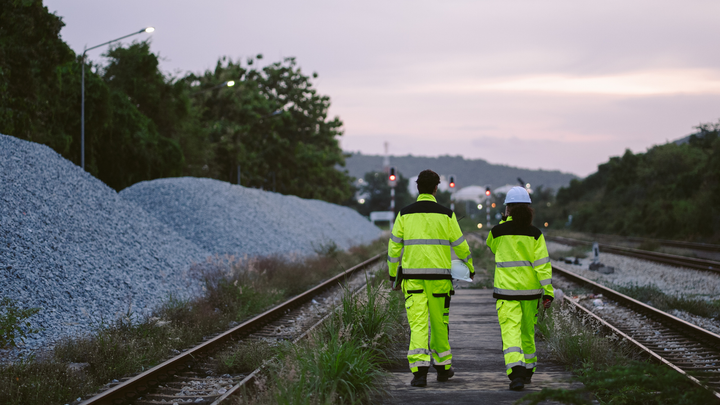 Two hi-vis workers walking along railway tracks at dusk during a site inspection.
