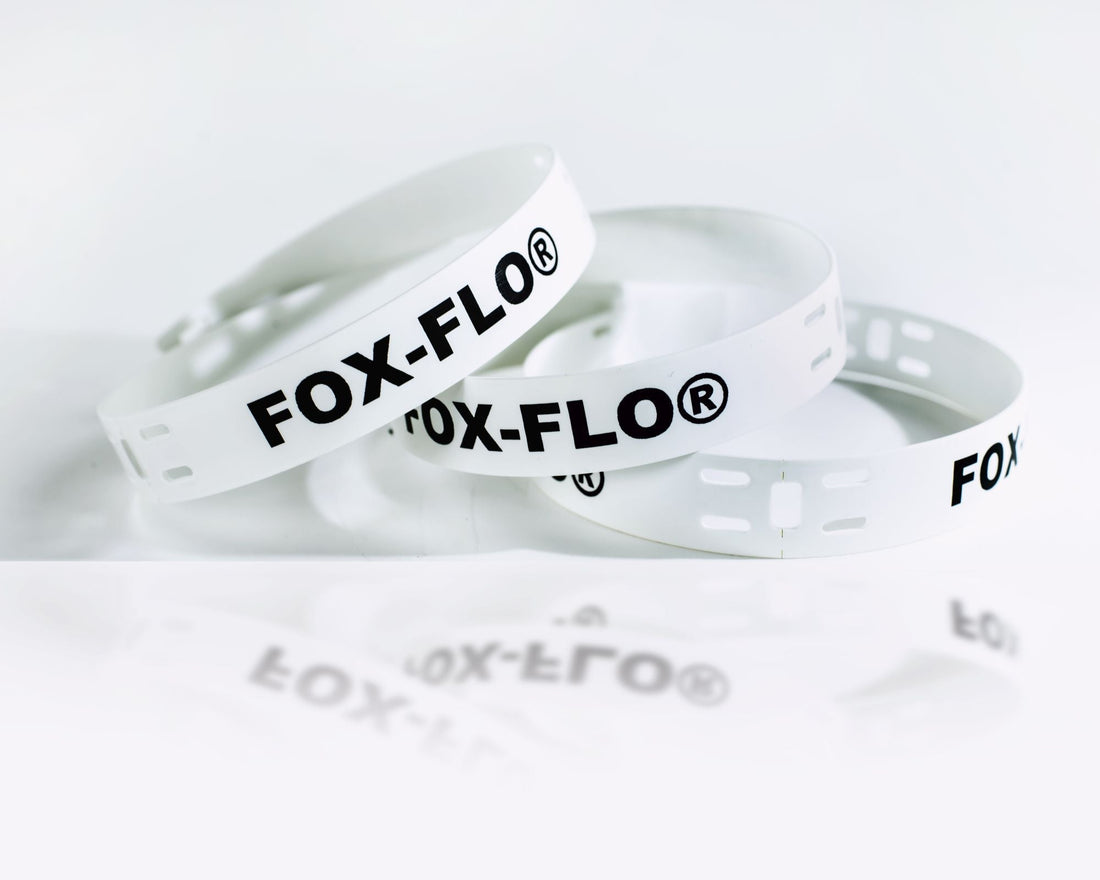 Coiled white cable marker strips printed with “FOX-FLO®” in bold black lettering lie on a clean white surface, with the slotted ends visible for fastening.